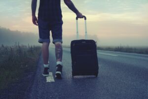 Man walking with a suitcase along a foggy road at sunrise, symbolizing adventure and travel.