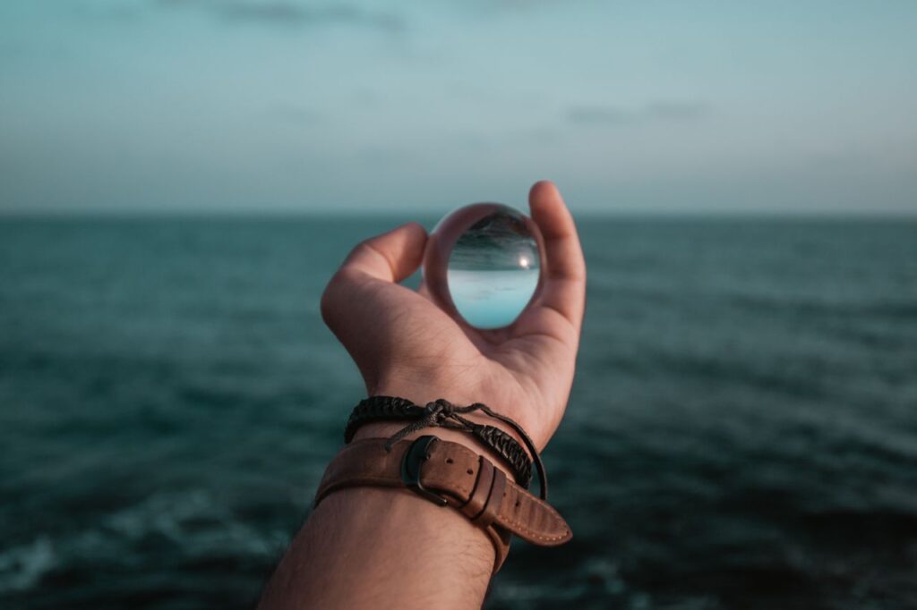 A hand holds a glass sphere reflecting the ocean horizon, creating a captivating visual effect.